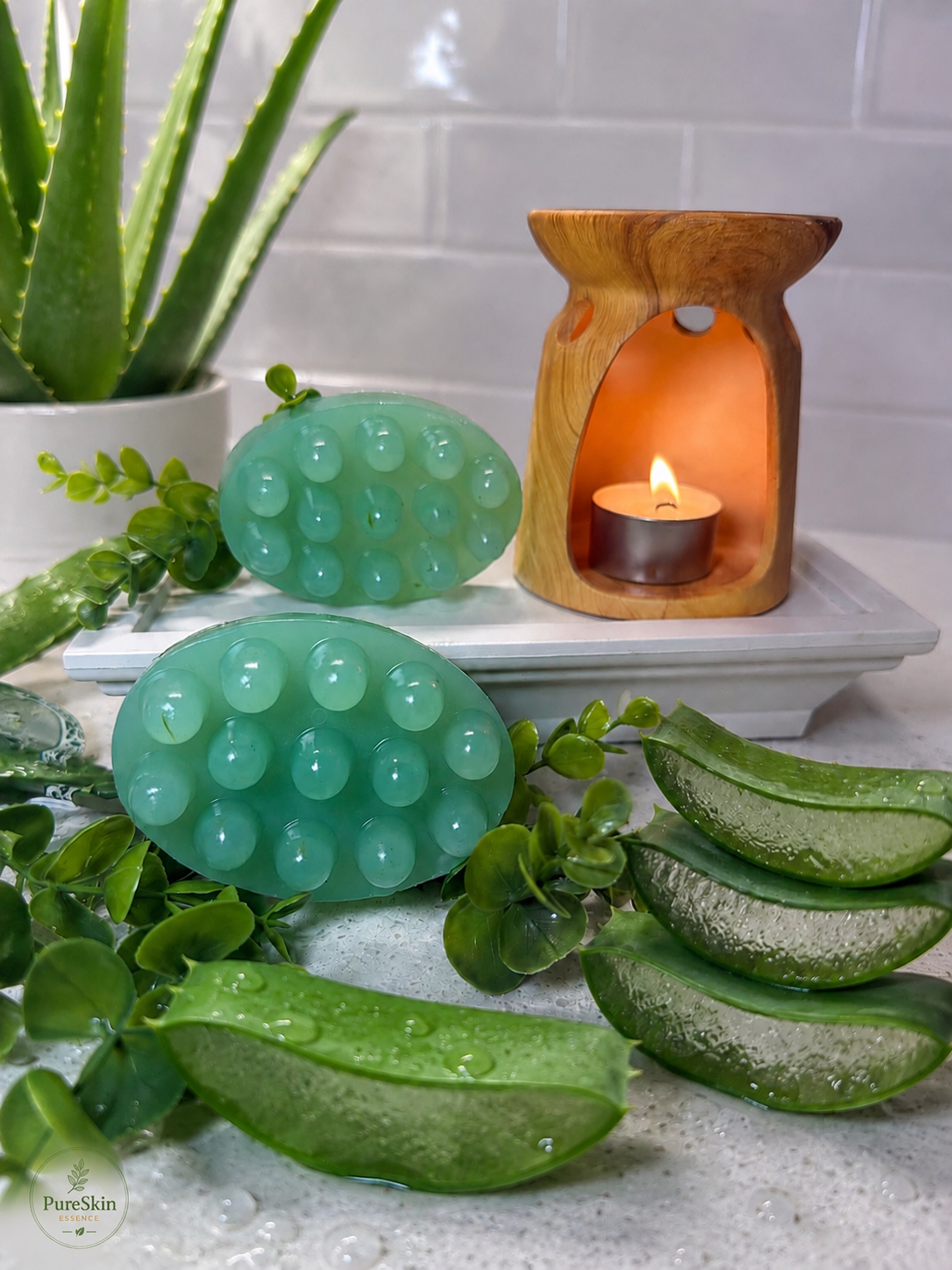 Wooden oil burner with a lit candle, surrounded by green decorative items and plants on a white surface.